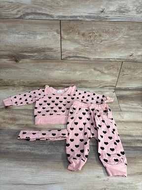 Pink baby outfit set with black heart patterns, including long-sleeve shirt, pants, and matching headband on wood floor