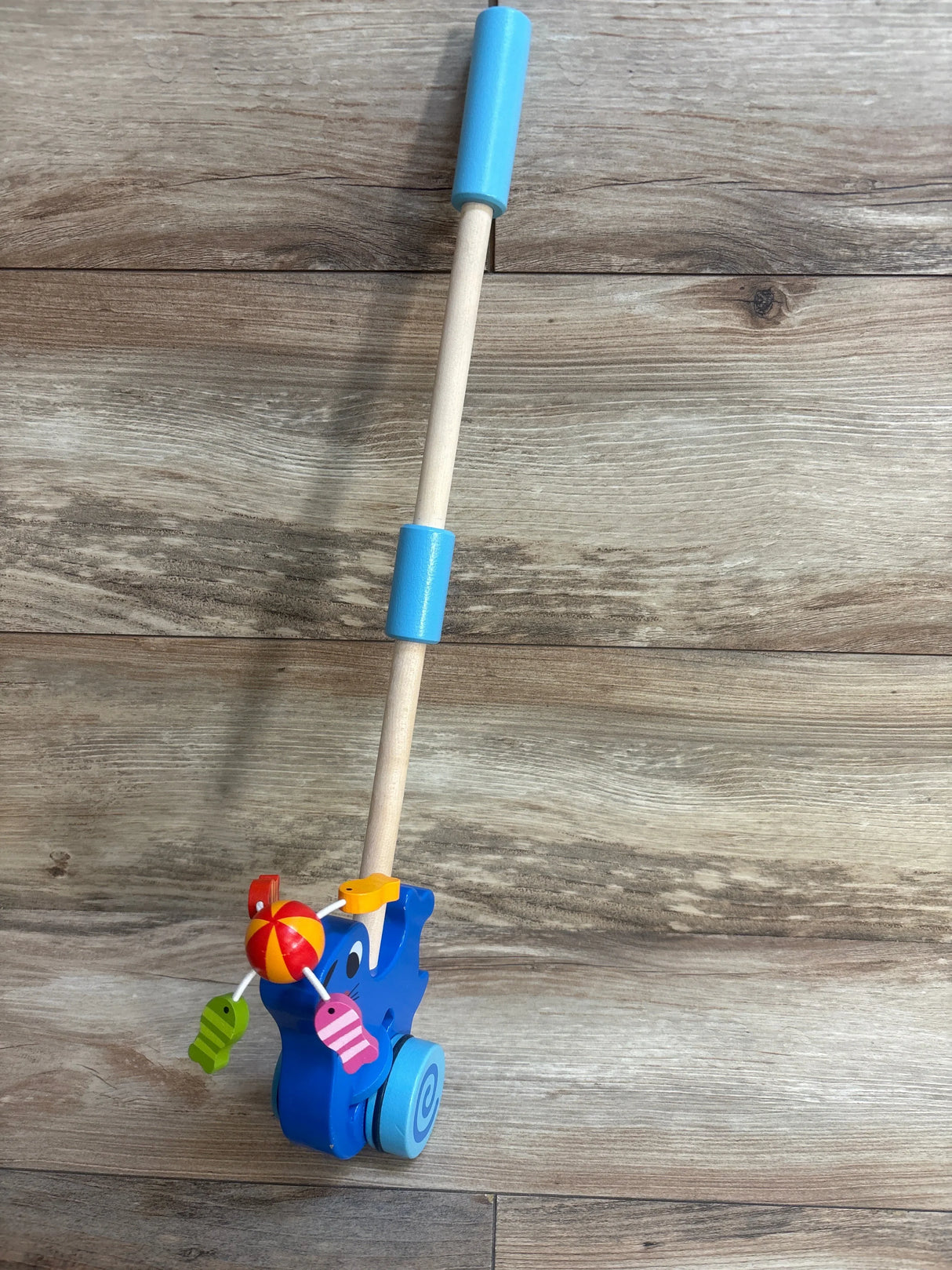 Wooden blue elephant push toy with colorful spinning ball and fish, on wood floor