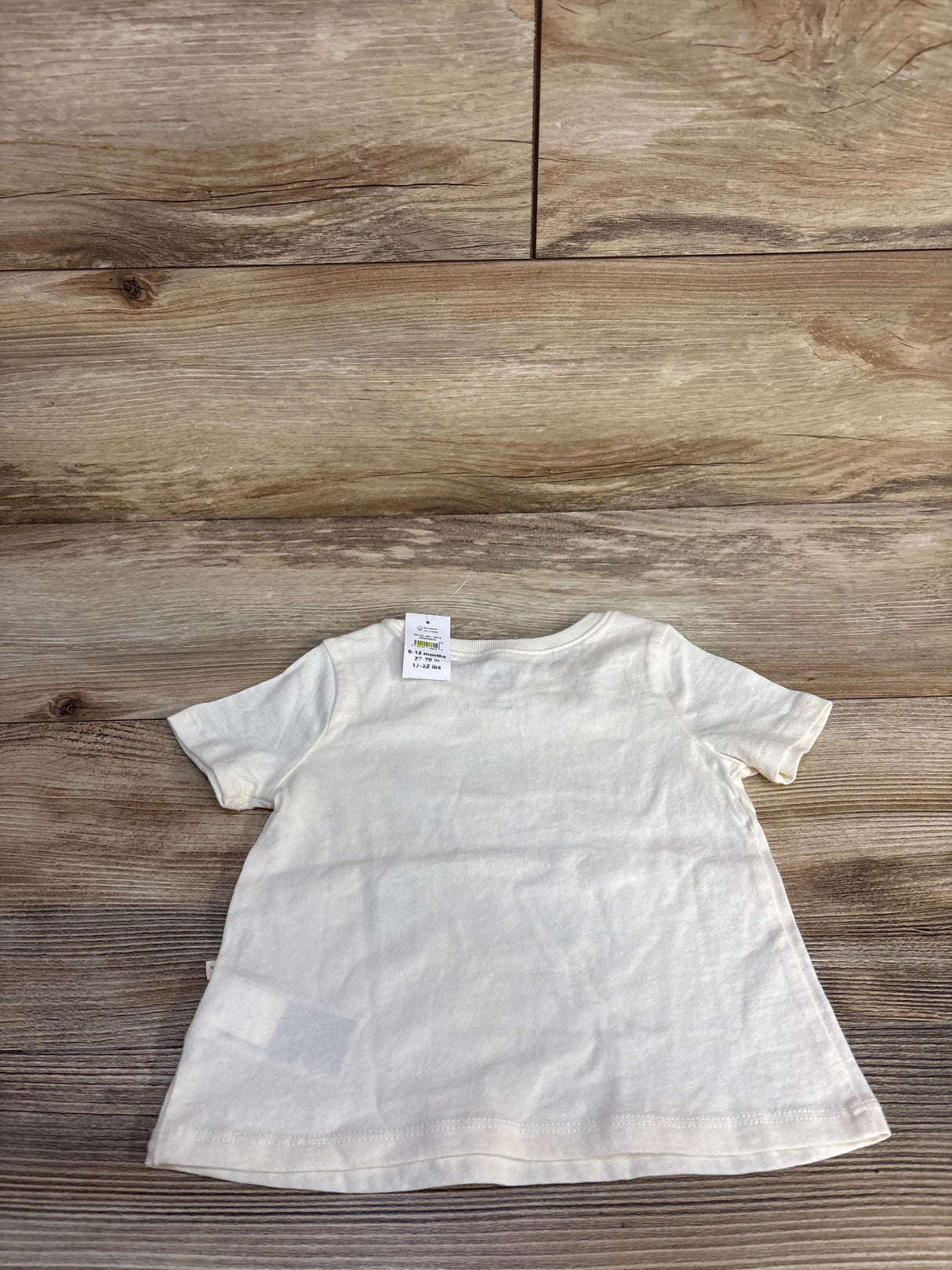 Back view of Baby Gap ivory short-sleeve baby shirt showing plain back and neck size tag on wood floor background