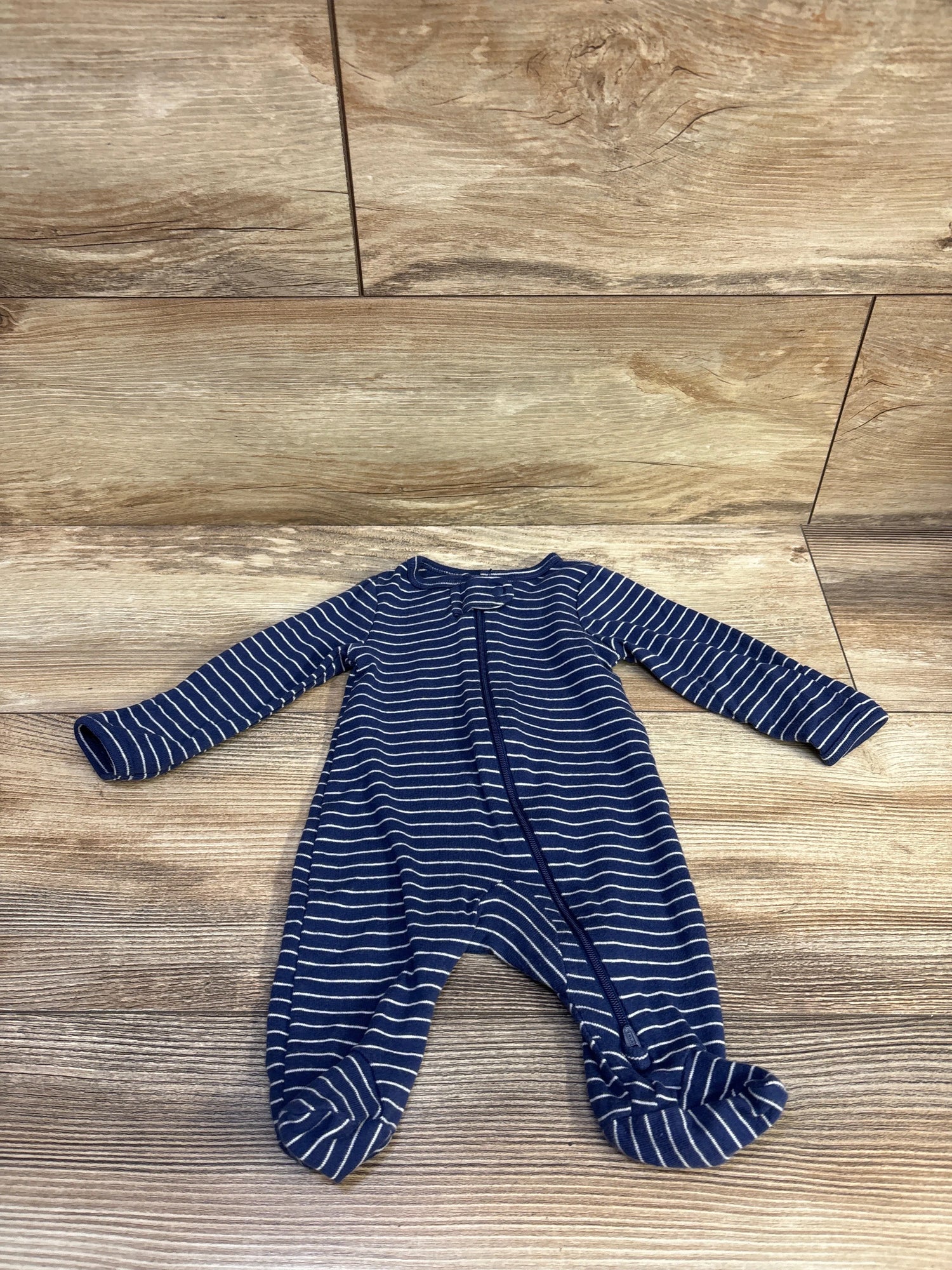 Front view of a blue striped newborn sleeper showcasing long sleeves, footed legs, and a front zipper on a wood-look floor