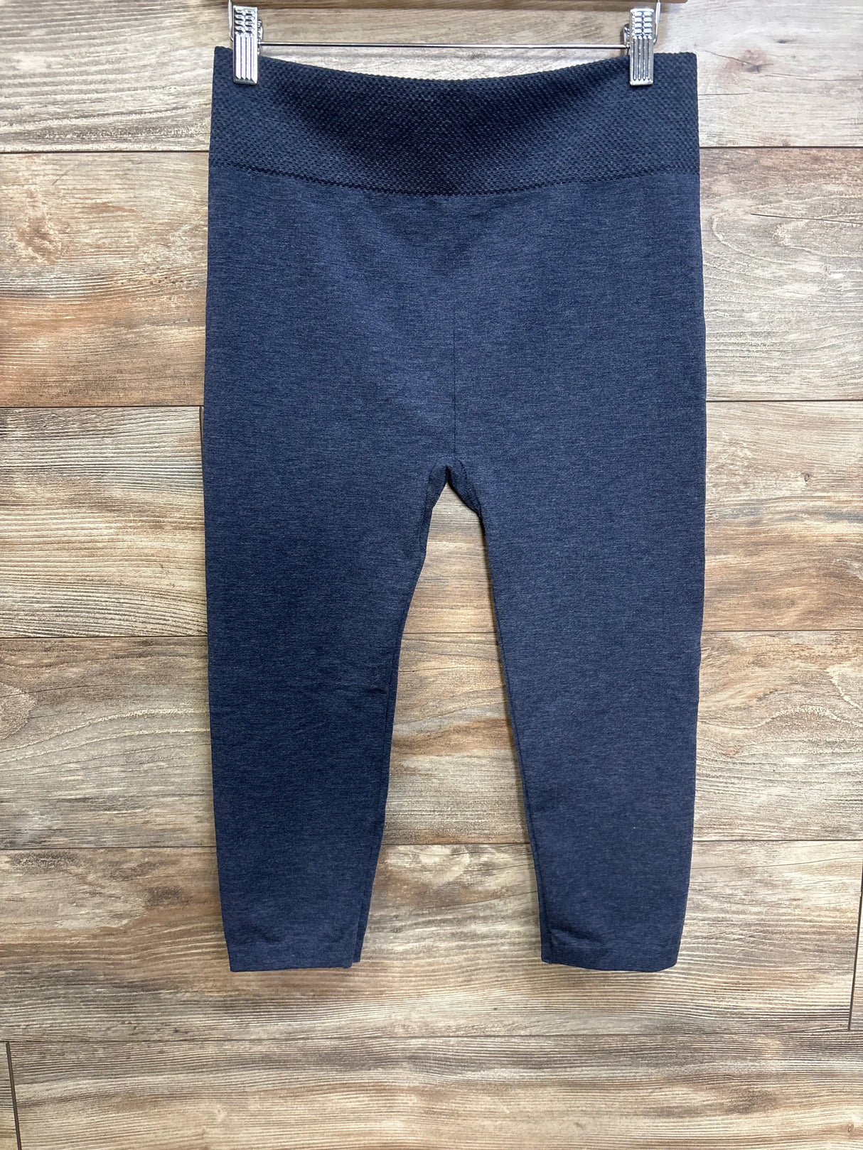 Front view of blue First Kick maternity leggings with high textured waistband and slim legs on wood background