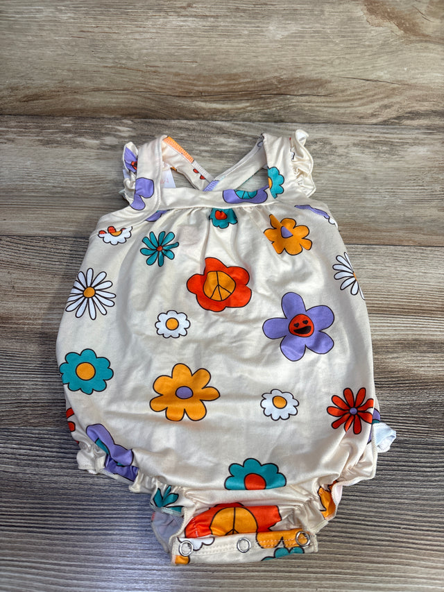 Top-down of beige Mila & Rose floral crossback romper with colorful flowers, ruffle straps, and snap crotch on light wood