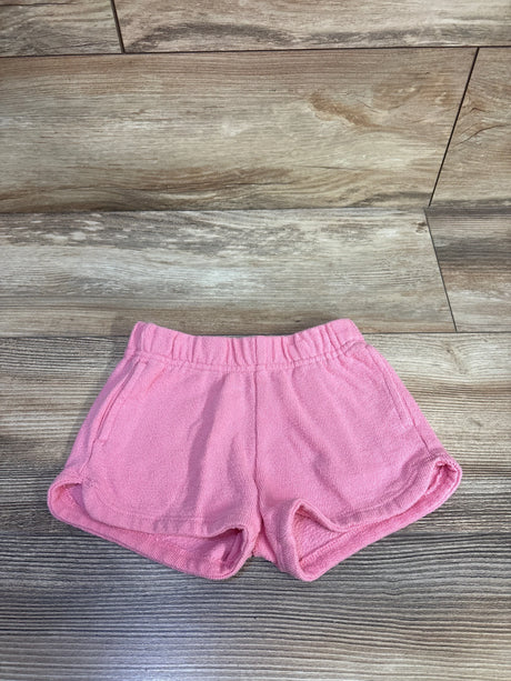 Top-down view of pink terry toddler shorts (2T) showing elastic waistband, side pockets, and curved hem on wood background