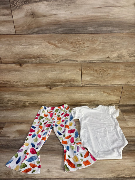 Flat-lay of white baby bodysuit and colorful bell-bottom pants set showing ruffle sleeves and elastic waist on wood floor