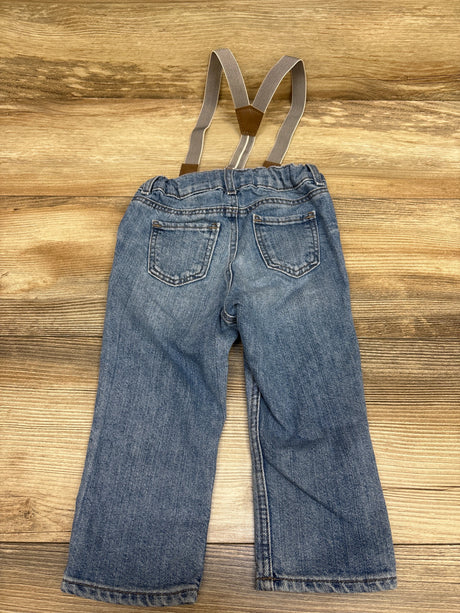 Rear view of H&M blue suspender jeans for 12 months showcasing two back pockets and adjustable suspenders on a wood background