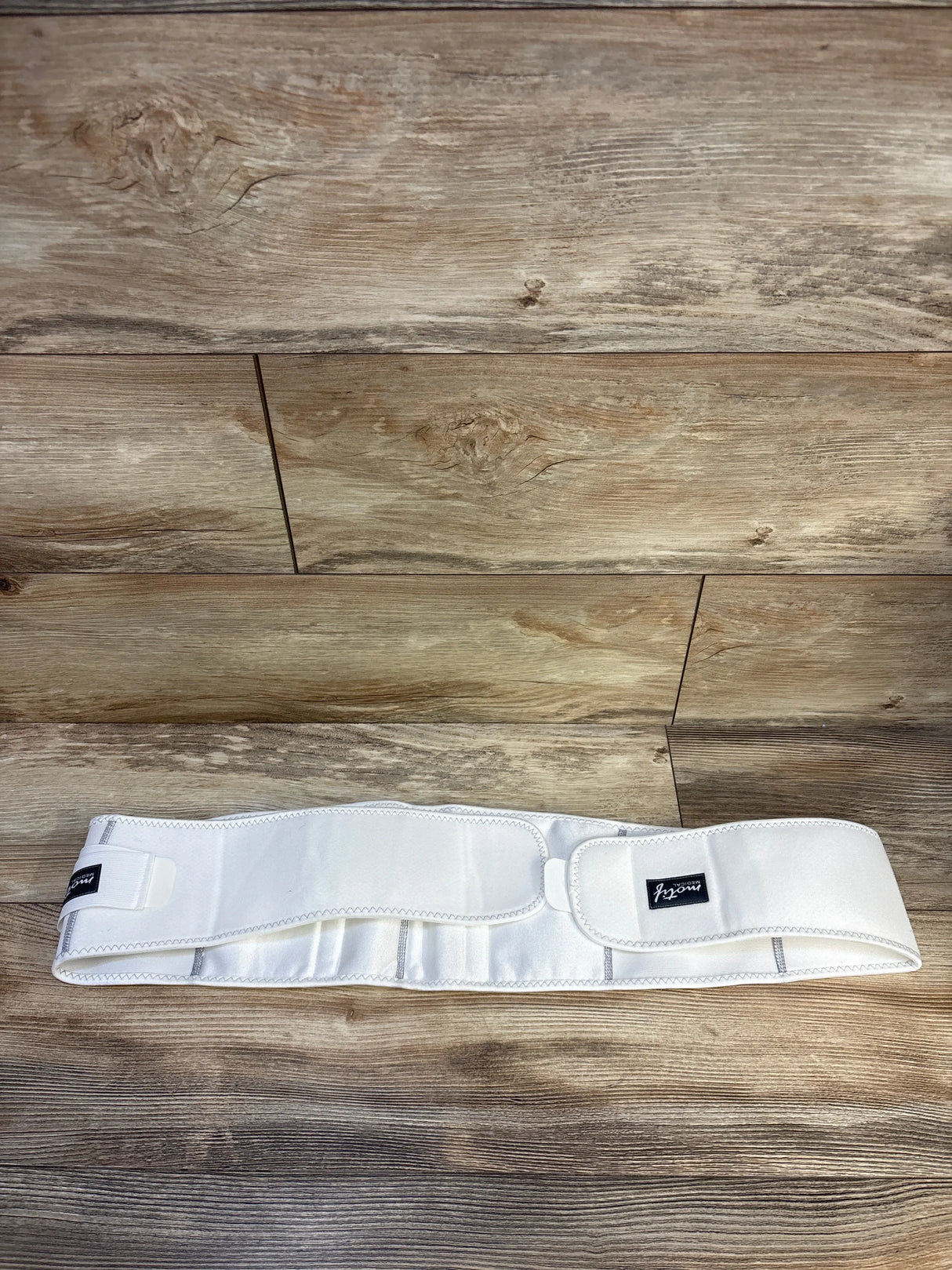White adjustable maternity belly support band on wood floor, kids resale store item