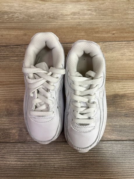 Top view of Nike Air Max 90 TD Triple White sneakers in size 9C with white laces and padded collars on wood grain