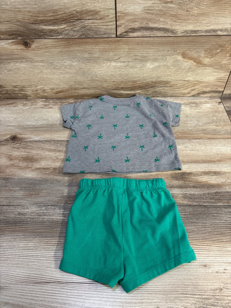 Flat lay of Cat & Jack 2-piece baby outfit: grey shirt with green palm trees and green elastic shorts, size 3-6 months, on wood background