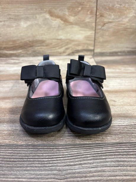 Front view of Stride Rite 360 Hazel Mary Jane flats showcasing black uppers and large bows with a wood-grain background