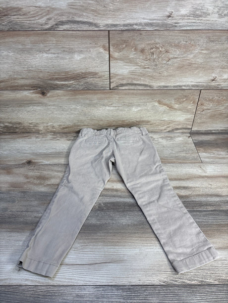 Flat lay back view of khaki toddler skinny stretch pants showing elastic waistband and back welt pockets on wood floor