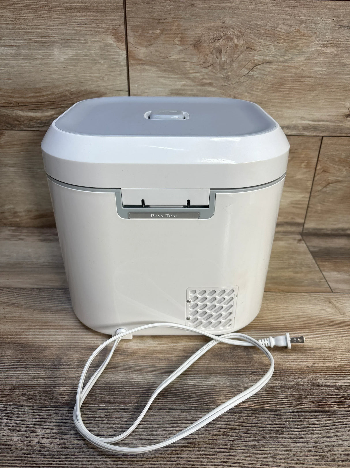 White electric diaper wipe warmer with power cord on wooden floor background