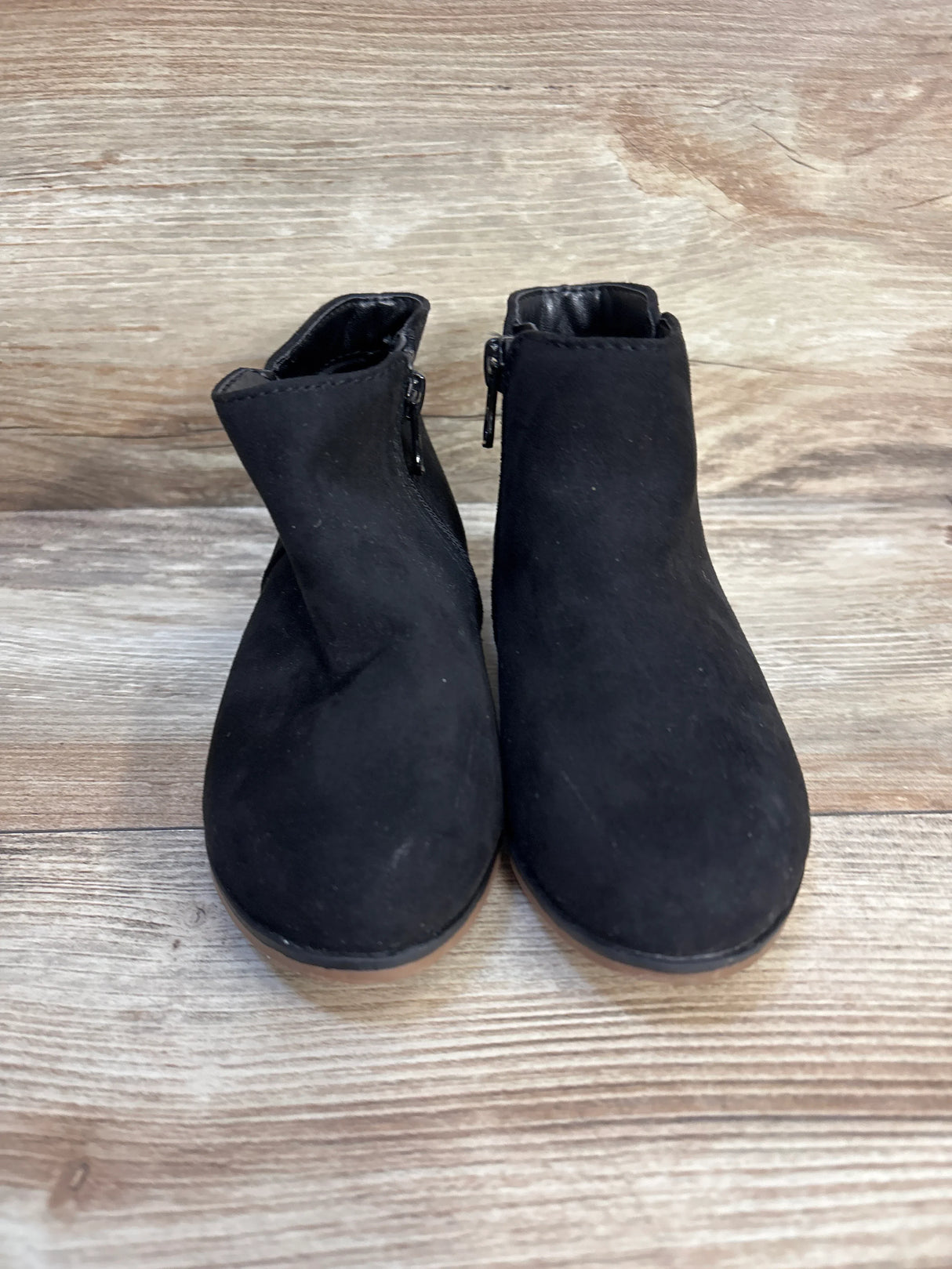 Pair of black suede children's ankle boots with side zippers on a wooden floor