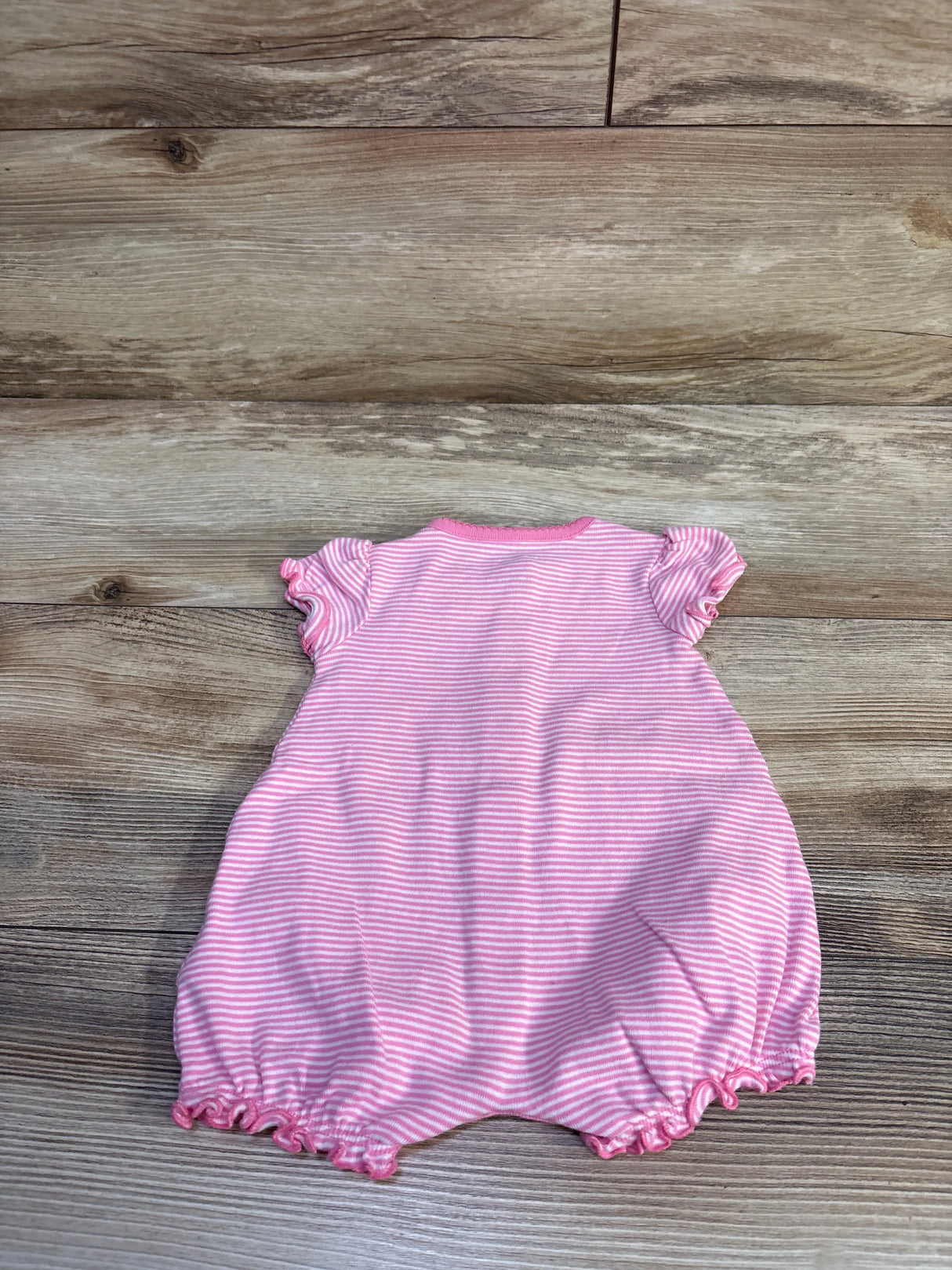 Back view of Simple Joys shortie romper in pink and white stripes showing ruffled cap sleeves and elastic ruffled leg openings on a light wood background