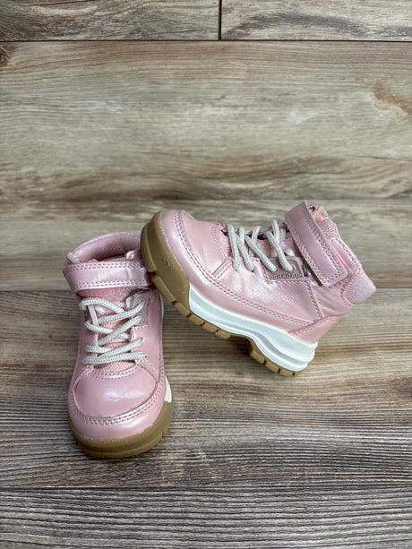 Pair of pink toddler boots with white laces and brown soles on wooden floor