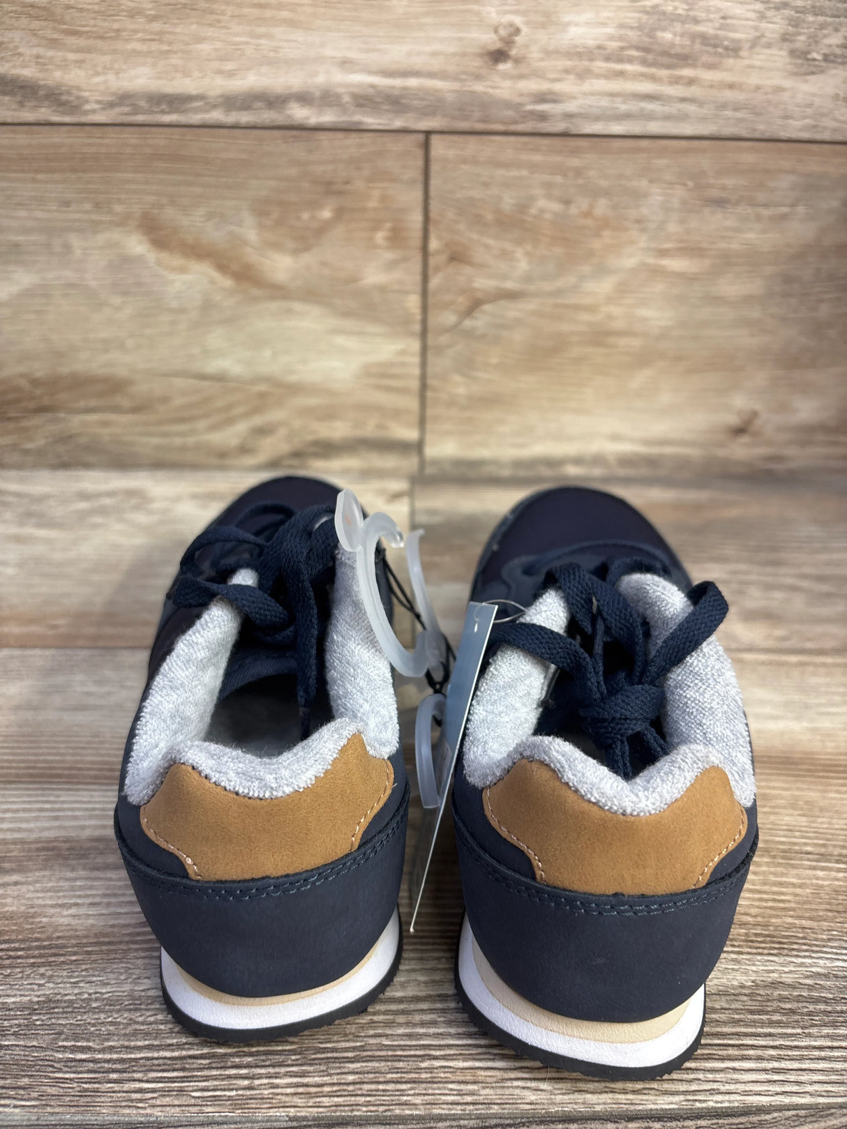 Rear view of Cat and Jack Jax toddler sneakers in navy blue showing tan heel accents, gray padded collar, and black laces on wood-grain background