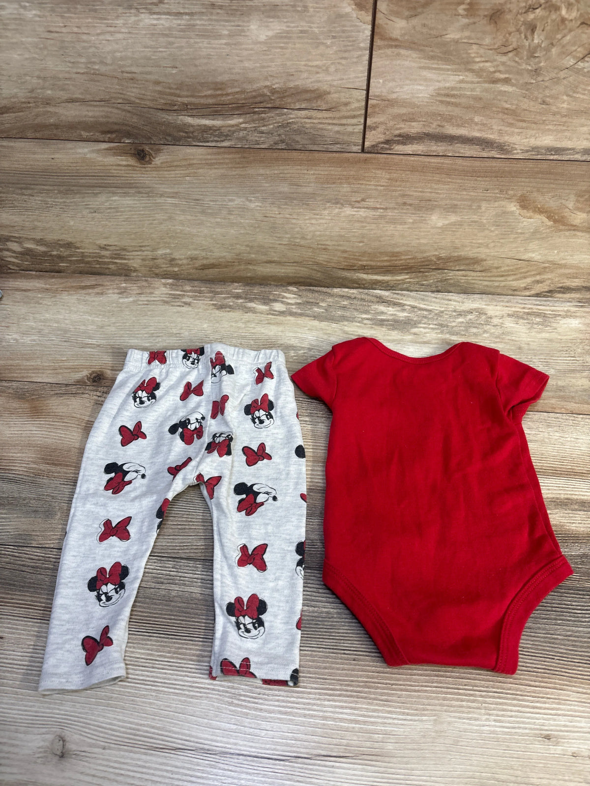 Top view of Disney Baby Minnie Mouse set showing red bodysuit and gray Minnie Mouse print pants on wood background