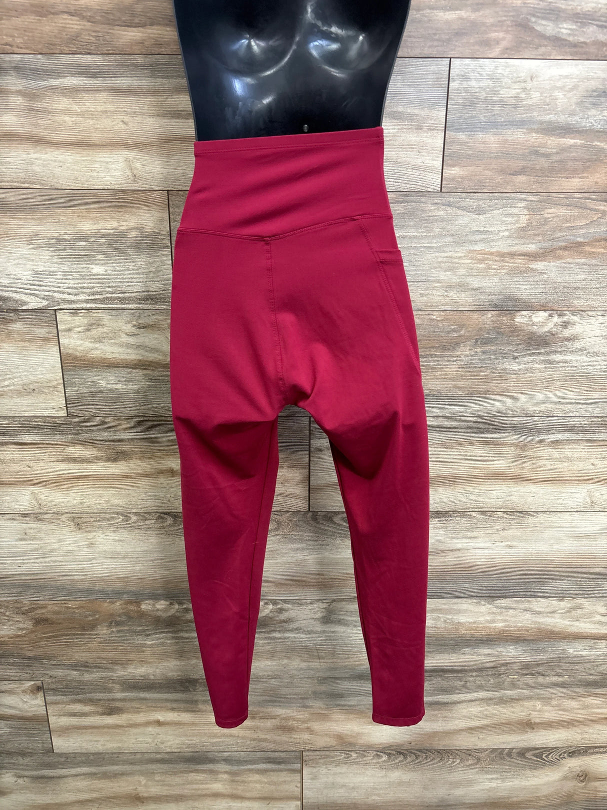 Front view of red maternity athletic leggings with high-rise belly panel and tapered ankles on mannequin with wood background