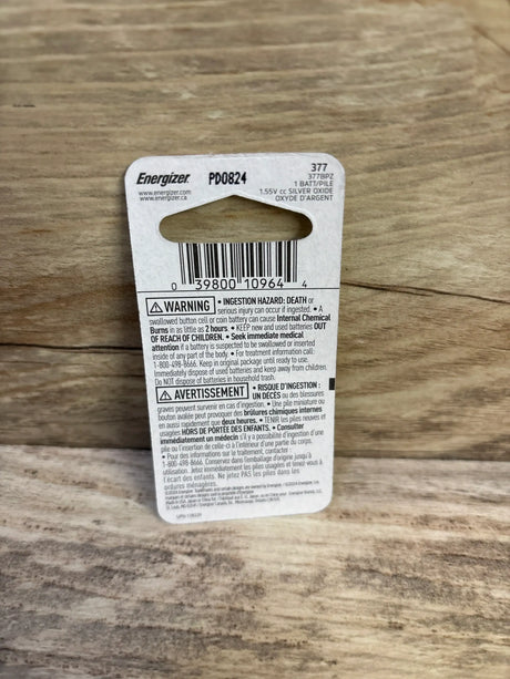 Back view of Energizer 377 button battery packaging showing barcode, warning text, and hang tab on wooden surface
