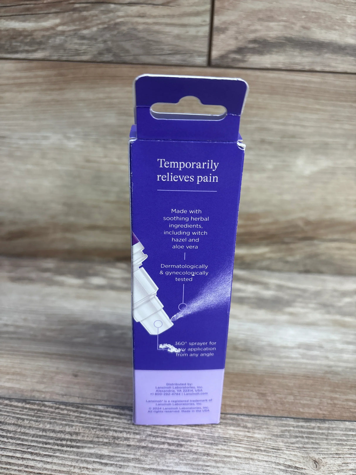 Rear view of Lansinoh postpartum spray box showing Temporarily relieves pain text and 360-degree sprayer graphic on wood