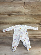 White baby onesie with purple birds, flowers, and bees on wooden floor