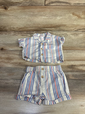 Flat lay of newborn striped button-up shirt and elastic-waist shorts showing red and blue stripes on cream wood background