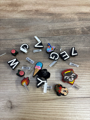 Crocs Jibbitz shoe charms with letters, ice cream, rose, raccoon, and cartoon character on wooden surface