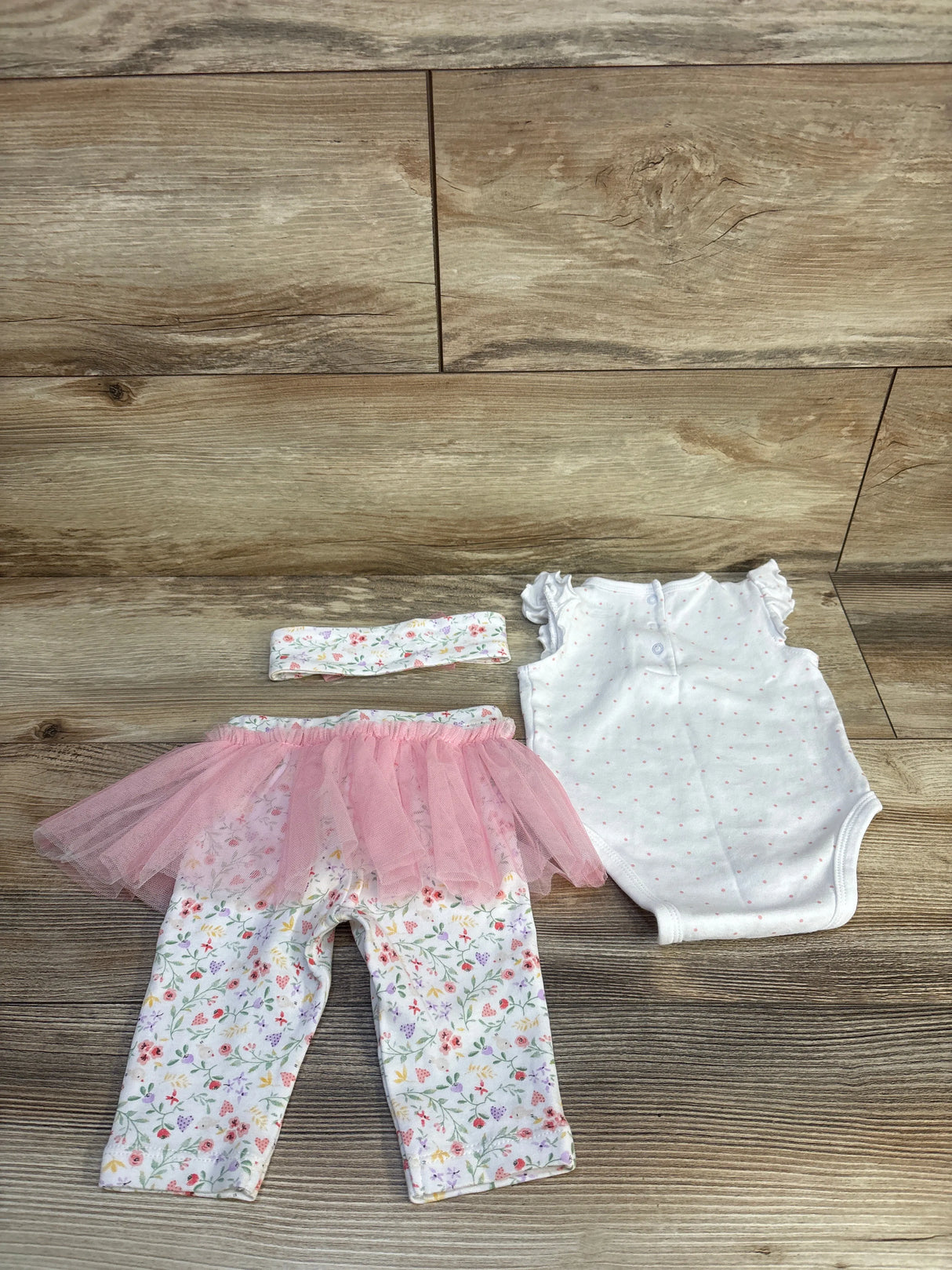 Baby outfit with floral pants, pink tutu, polka dot onesie, and matching headband on wood floor