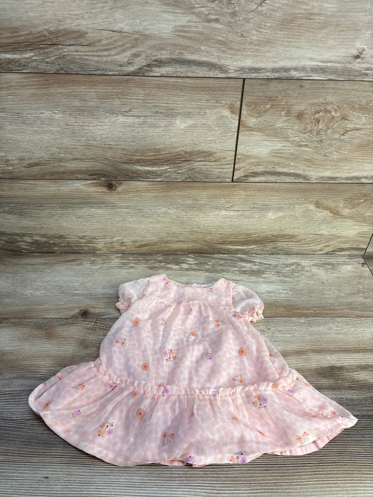 Flat lay of pink floral baby dress showcasing puff sleeves and ruffled hem on light wood background