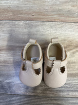 Top-down view of beige First Steps soft-sole baby shoes showing scalloped T-strap and star-shaped cutouts on gray wood floor
