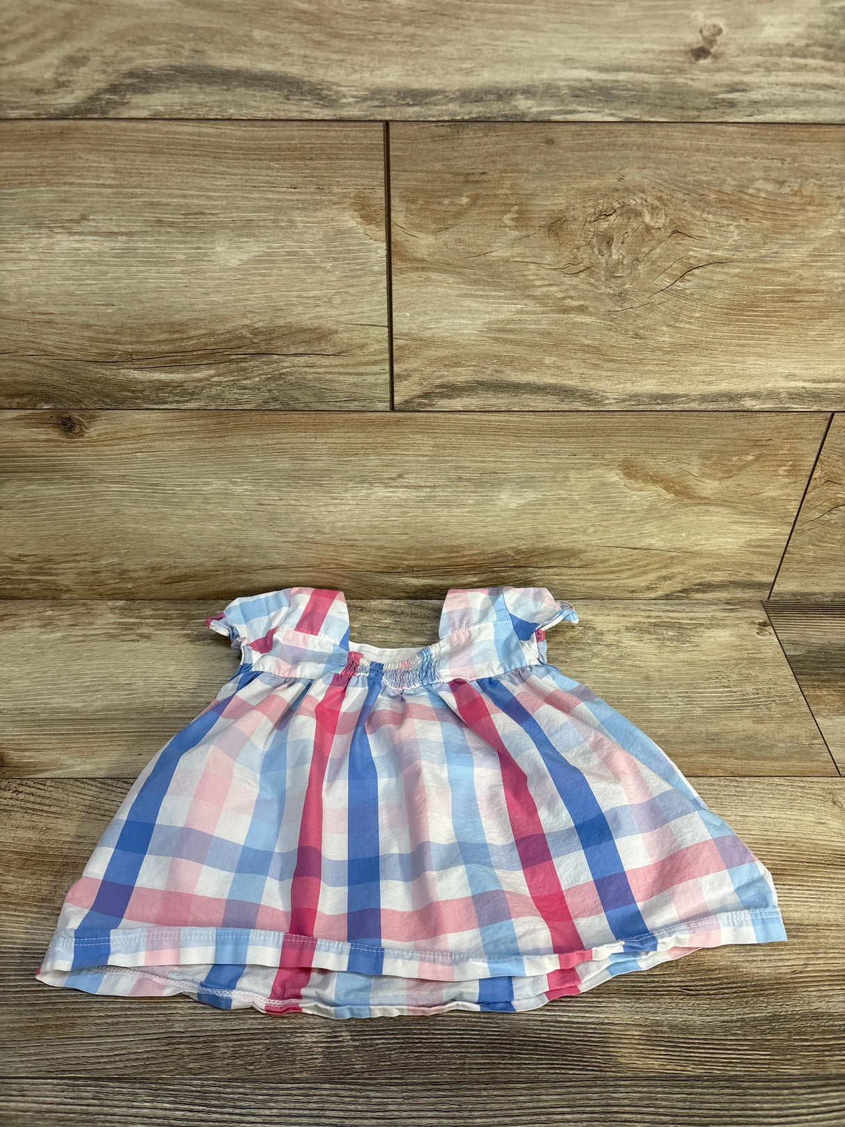 Pink and blue plaid baby dress with ruffled sleeves on wood background