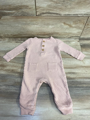 Textured pink baby romper with wooden buttons and front pockets on wooden background
