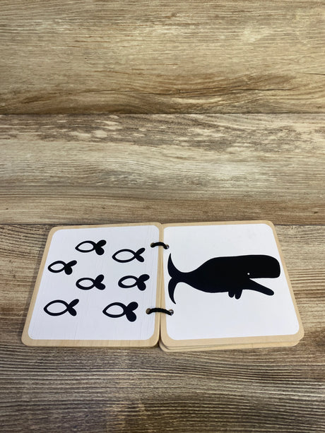 Open view of Lovevery wooden board book showcasing black-and-white whale illustration and fish icons on wood tabletop background