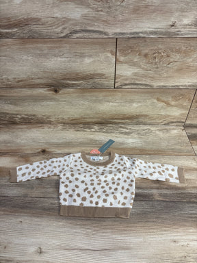 Baby sweater with tan polka dot pattern, long sleeves, and ribbed trim on wooden background