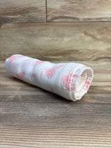 Angled view of a rolled white GLLQUEN muslin bamboo swaddle blanket showcasing pink printed motifs on a wood surface