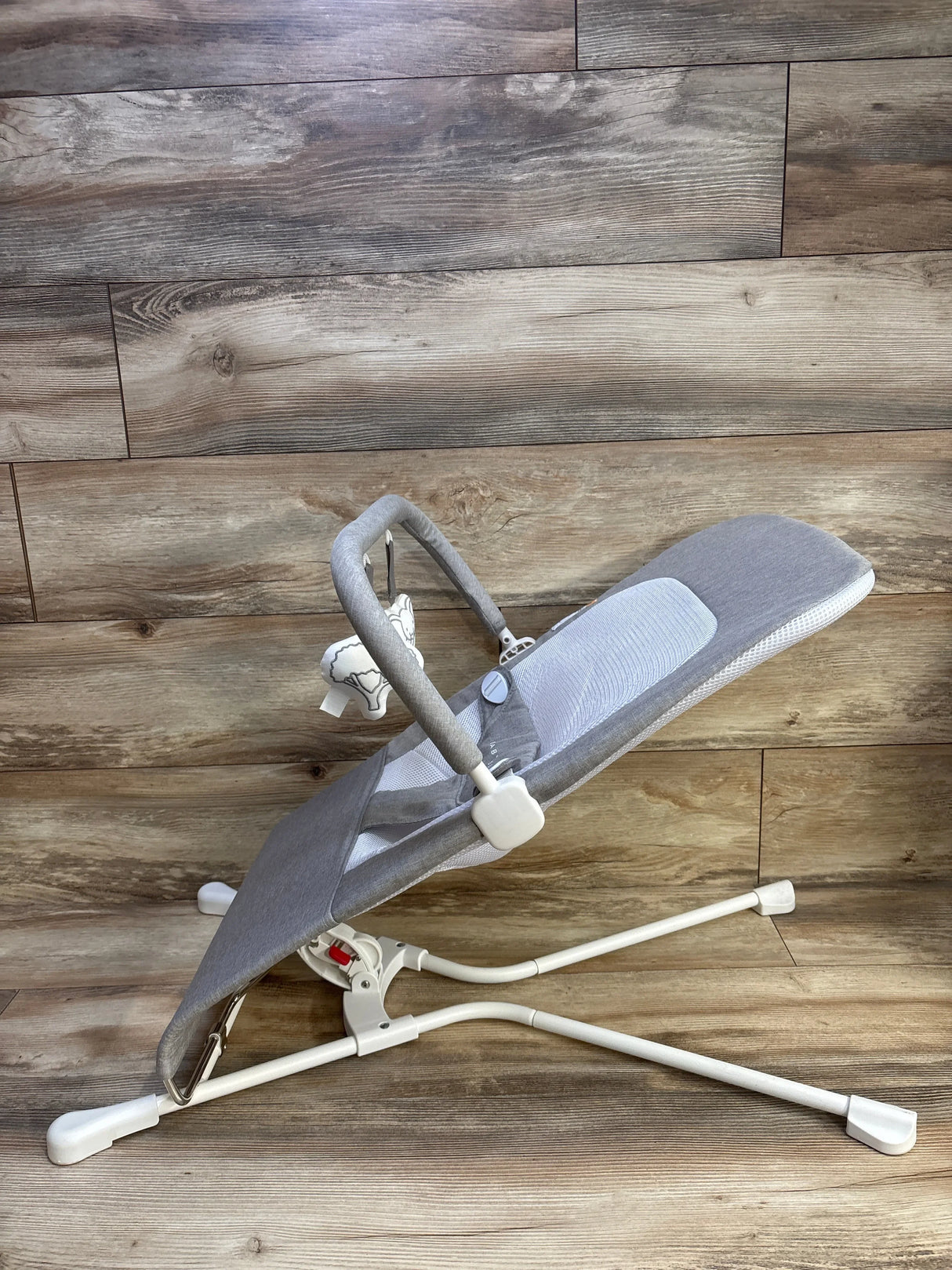 Side view of Baby Delight Highland bouncer showing pebble grey fabric, mesh seat, toy bar with plush, white frame