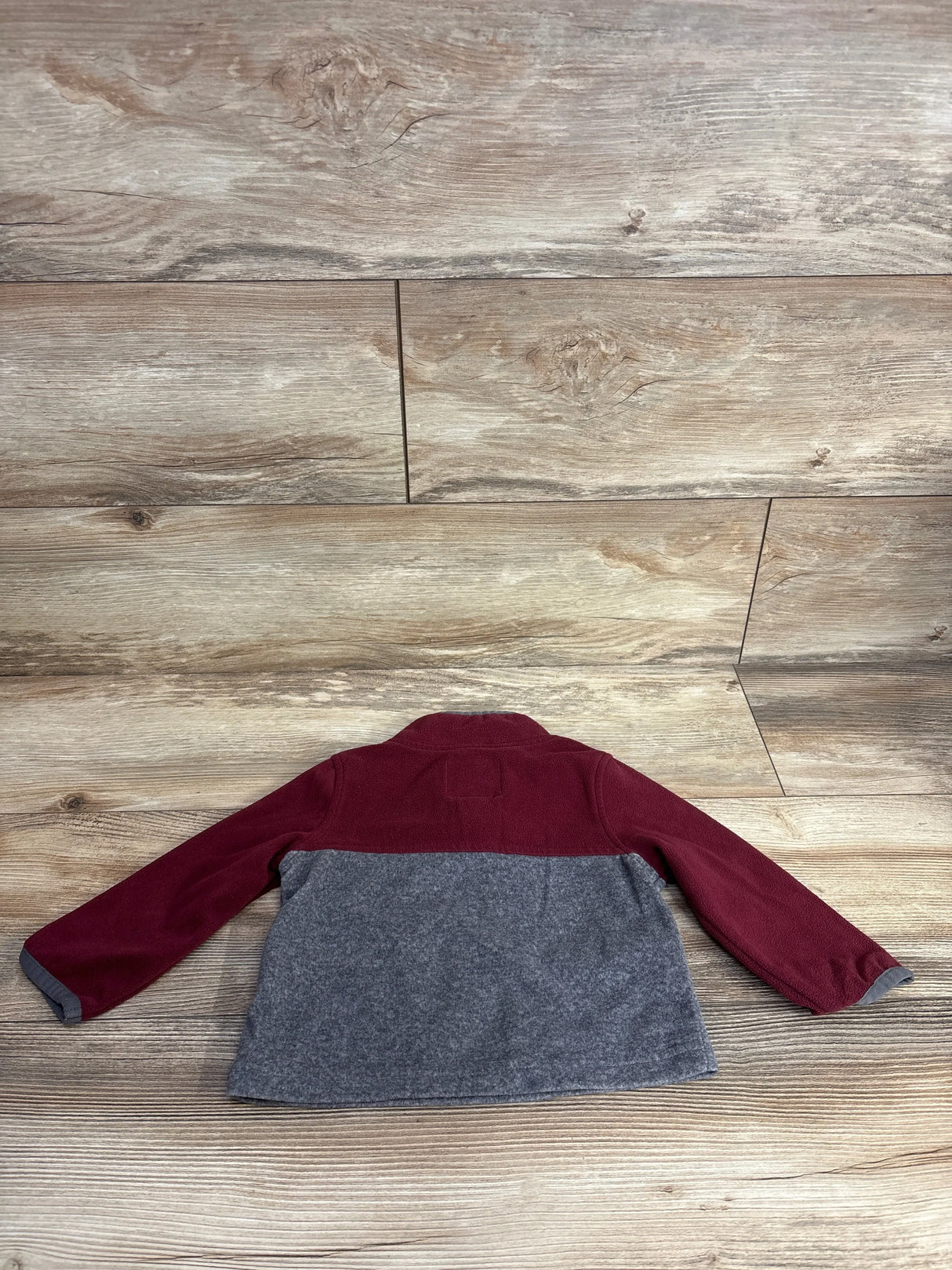 Kids fleece jacket with maroon sleeves and gray body laid flat on wooden surface