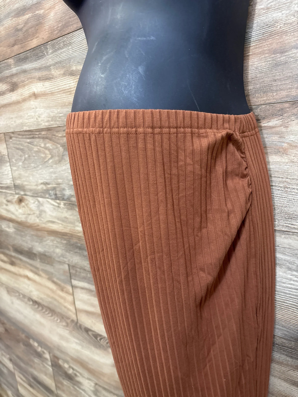 Side view of brown ribbed maternity skirt with elastic waistband on mannequin against wood background