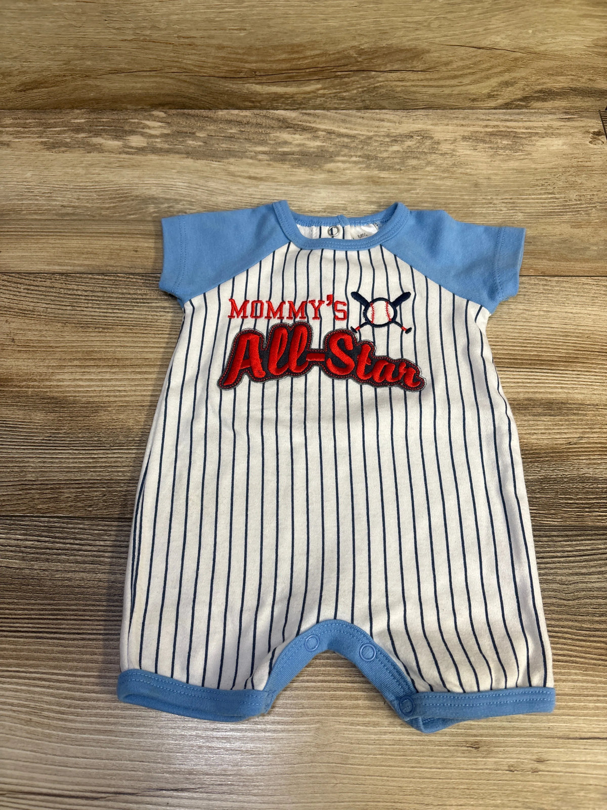 Front view of Little Beginnings Mommy’s All Star shortie romper with blue trim, baseball graphic, and vertical pinstripes on wood