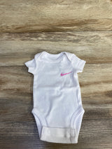 Front view of newborn white Nike bodysuit showing pink Nike swoosh on chest, laid flat on wood background