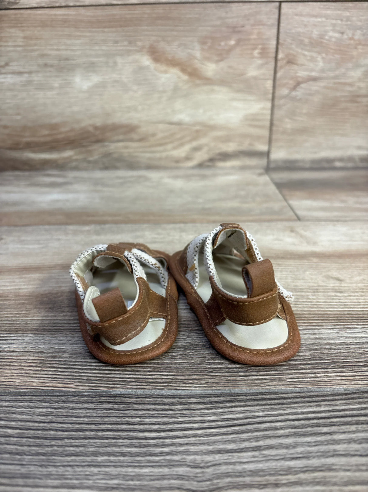 Front view of Cat and Jack tan soft-sole baby sandals showing Velcro ankle strap and white footbed on wood background