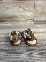 Front view of Cat and Jack tan soft-sole baby sandals showing Velcro ankle strap and white footbed on wood background
