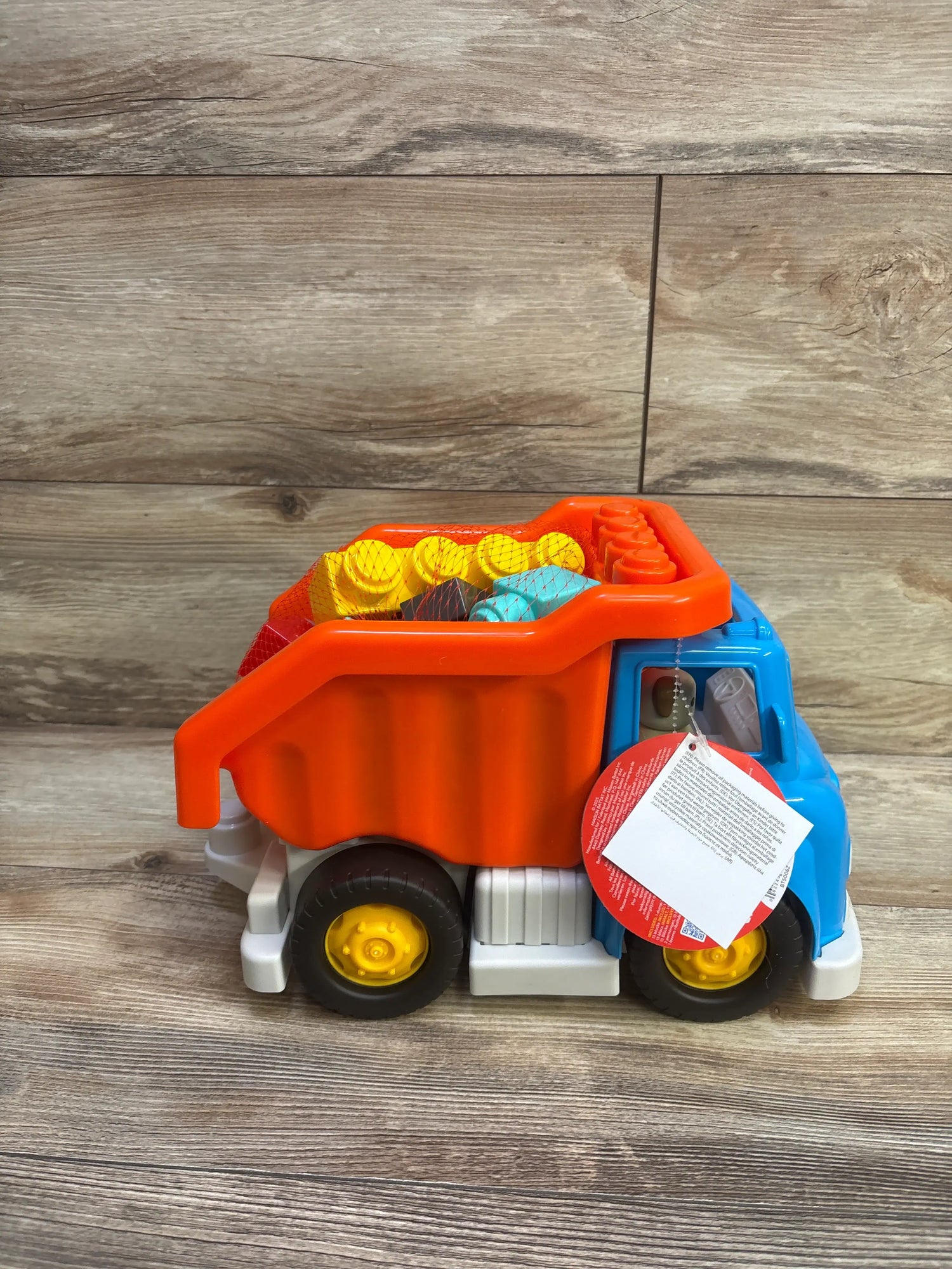 Side view of Battat dump truck with orange bed, blue cab, yellow wheels, and 17 building blocks on a wood floor