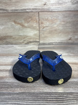 Front view of Locals toddler flip-flops with translucent blue straps, black soles and gold 7.5 stickers on wood background