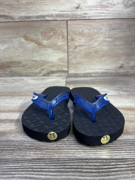 Front view of Locals toddler flip-flops with translucent blue straps, black soles and gold 7.5 stickers on wood background