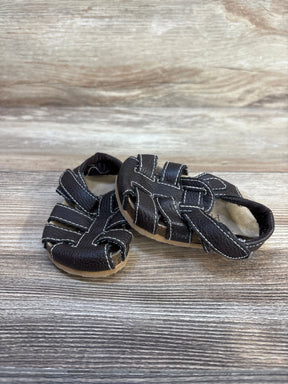 Angled front view of Children's Place brown leather fisherman sandals showing woven straps, white contrast stitching and tan sole on wood background