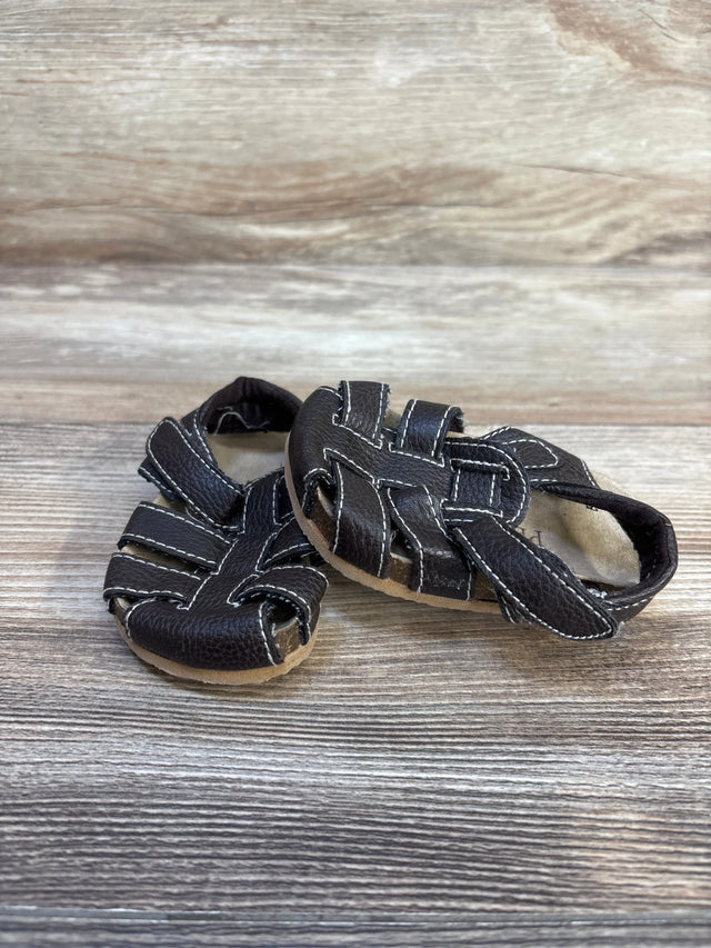 Angled front view of Children's Place brown leather fisherman sandals showing woven straps, white contrast stitching and tan sole on wood background