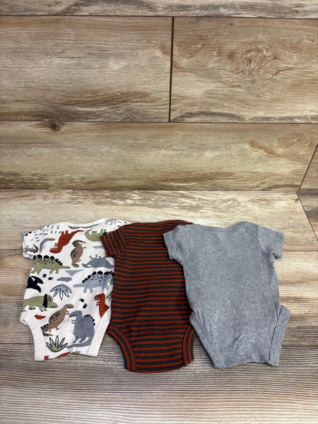 Front view of three Gerber newborn bodysuits showcasing dinosaur print, orange stripes, and solid gray fabric on a wood surface