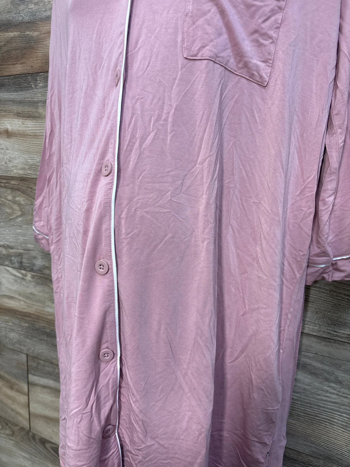 Front close-up of pink Caden Lane maternity nightgown showing buttons, white piped trim and chest pocket on wood background
