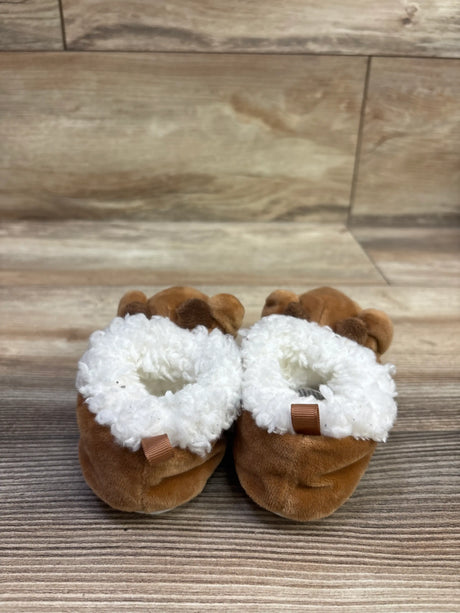 Front view of brown Rudolph the Red-Nosed Reindeer plush slippers with white fluffy lining and reindeer antlers on a wood floor