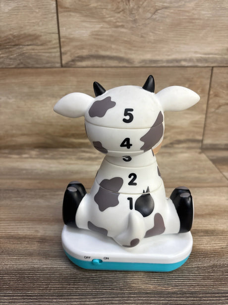 Back view of Stack-a-Roos Baby Cow showcasing numbered 1-5 stackable sections, gray spots and teal base on wood tabletop